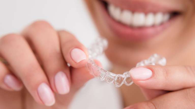 A smiling woman holding an Invisalign tray
